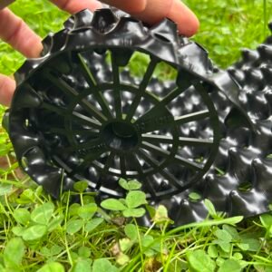 Ruka drží černou plastovou podložku na trávě.