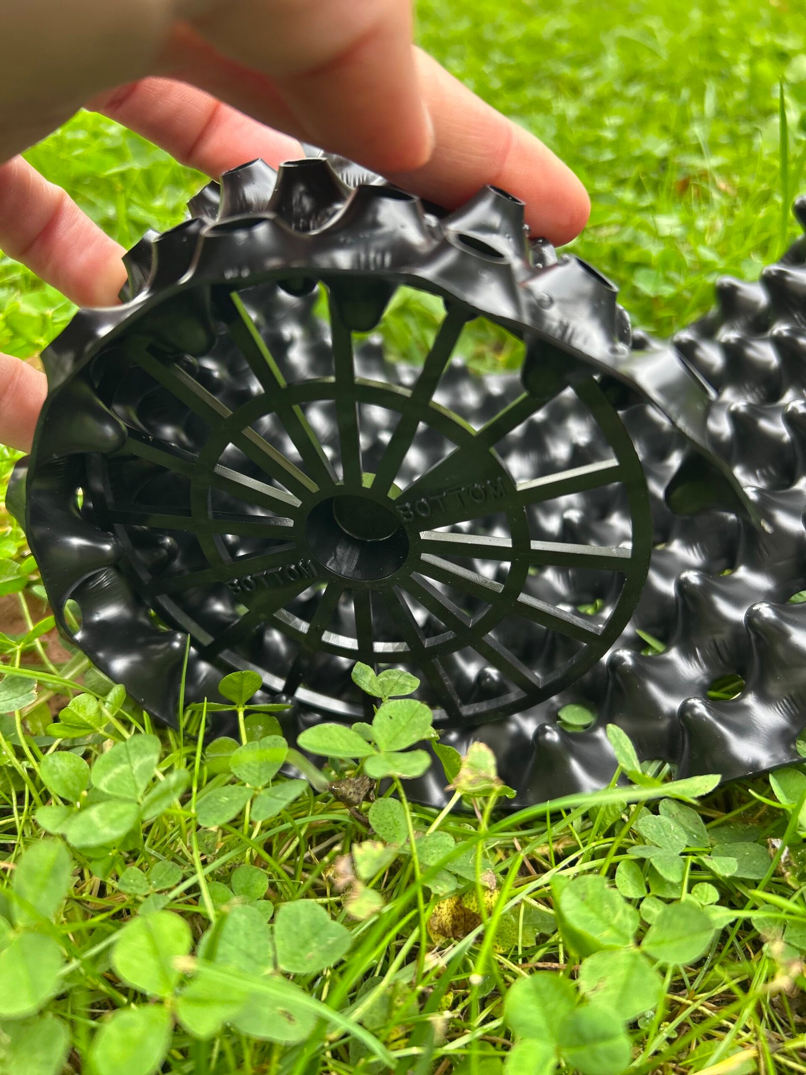 Ruka drží černou plastovou podložku na trávě.